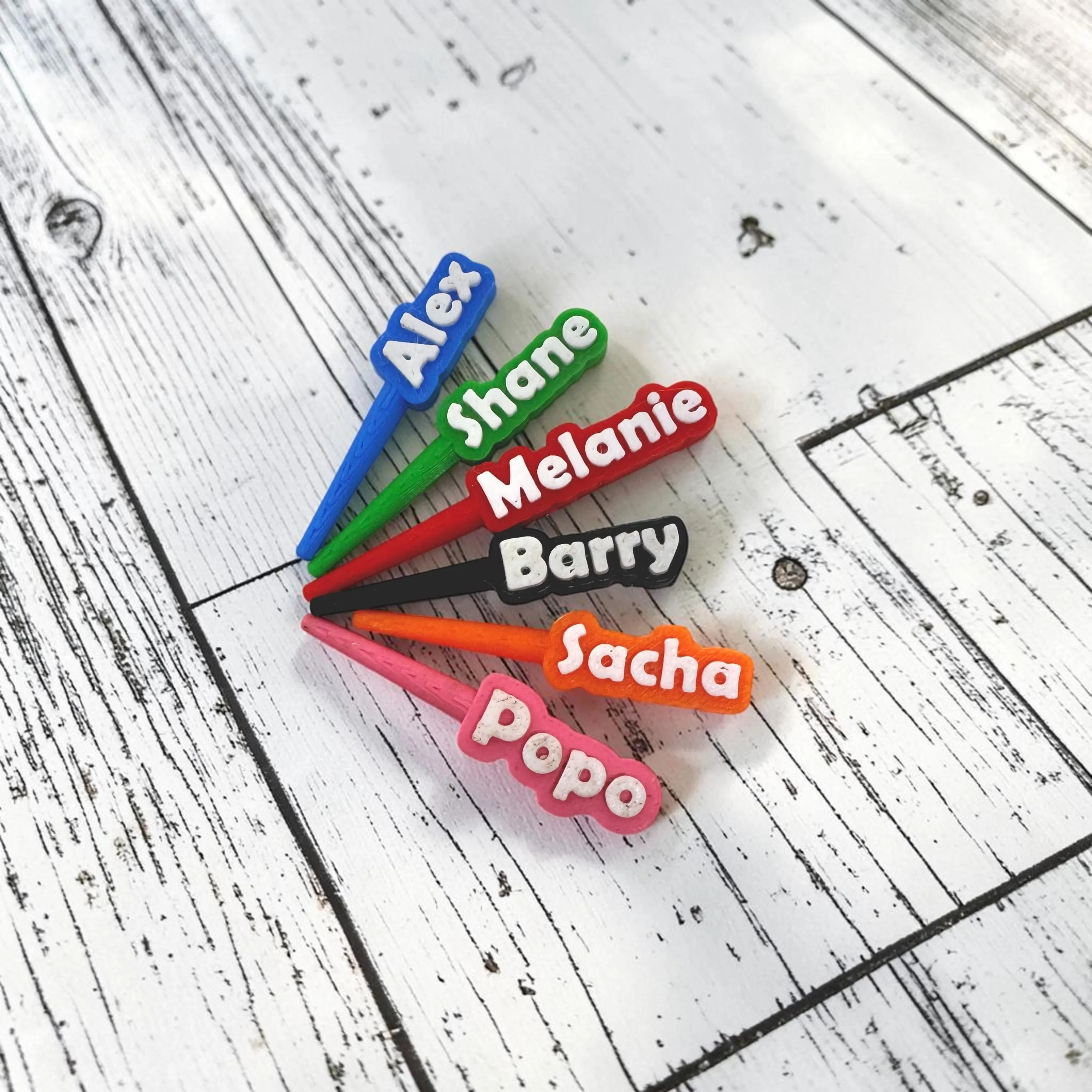 Personalized pegs engraved with names, in six colors: blue, green, red, black, orange, and pink