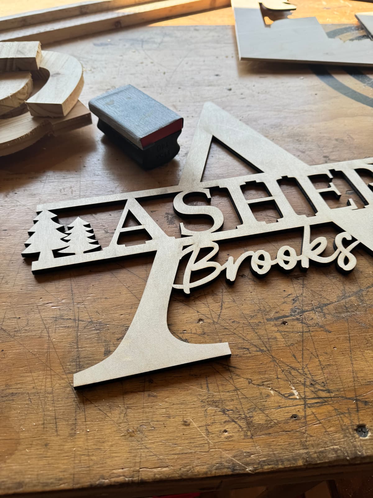Freshly CNC-cut wooden 'Home Sweet Home' sign with pine tree detail, still on the workbench