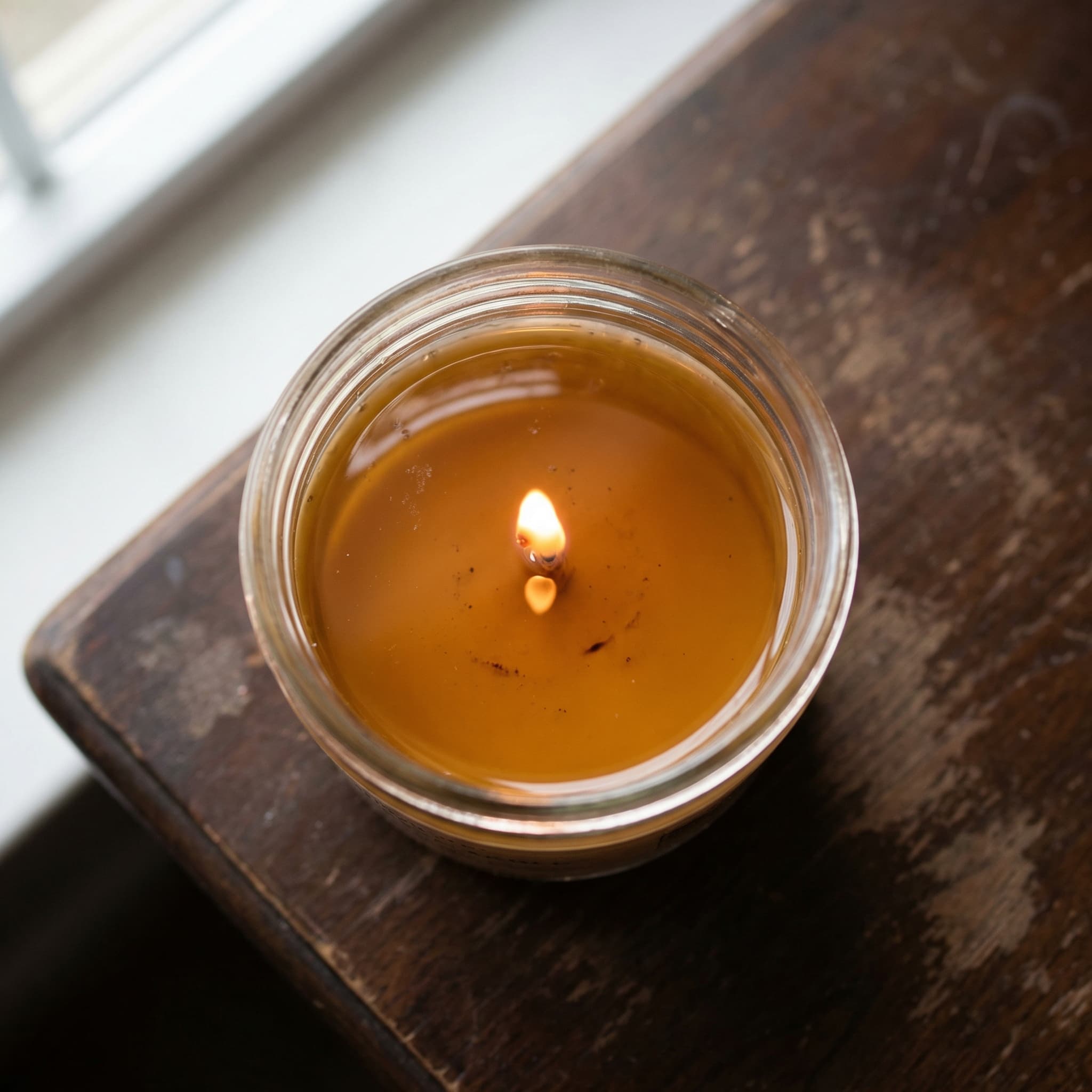 Top-down view of a lit candle with a full edge-to-edge melt pool