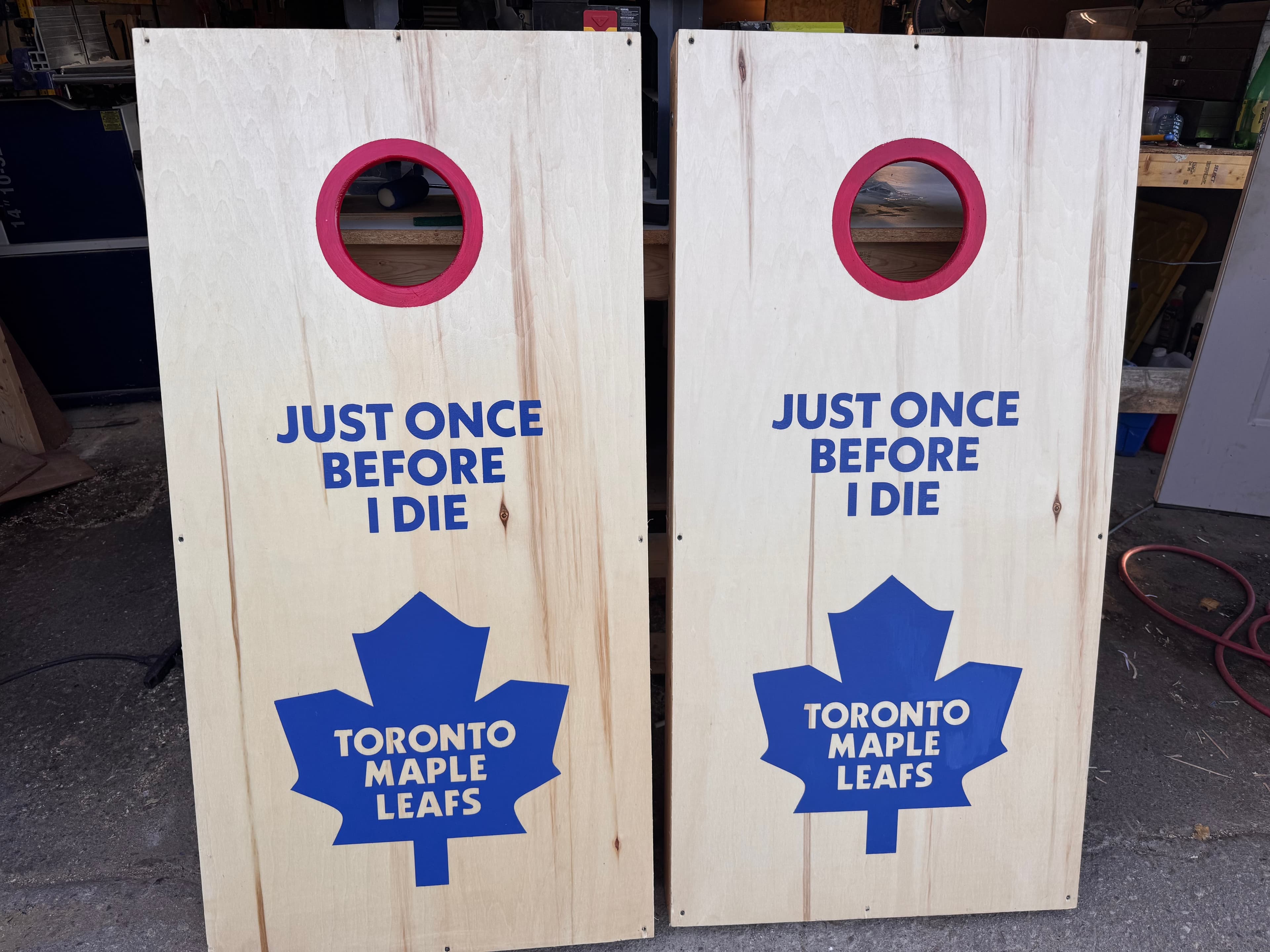 Two cornhole boards standing upright side by side with Toronto Maple Leafs logo and text reading JUST ONCE BEFORE I DIE in blue vinyl on natural birch