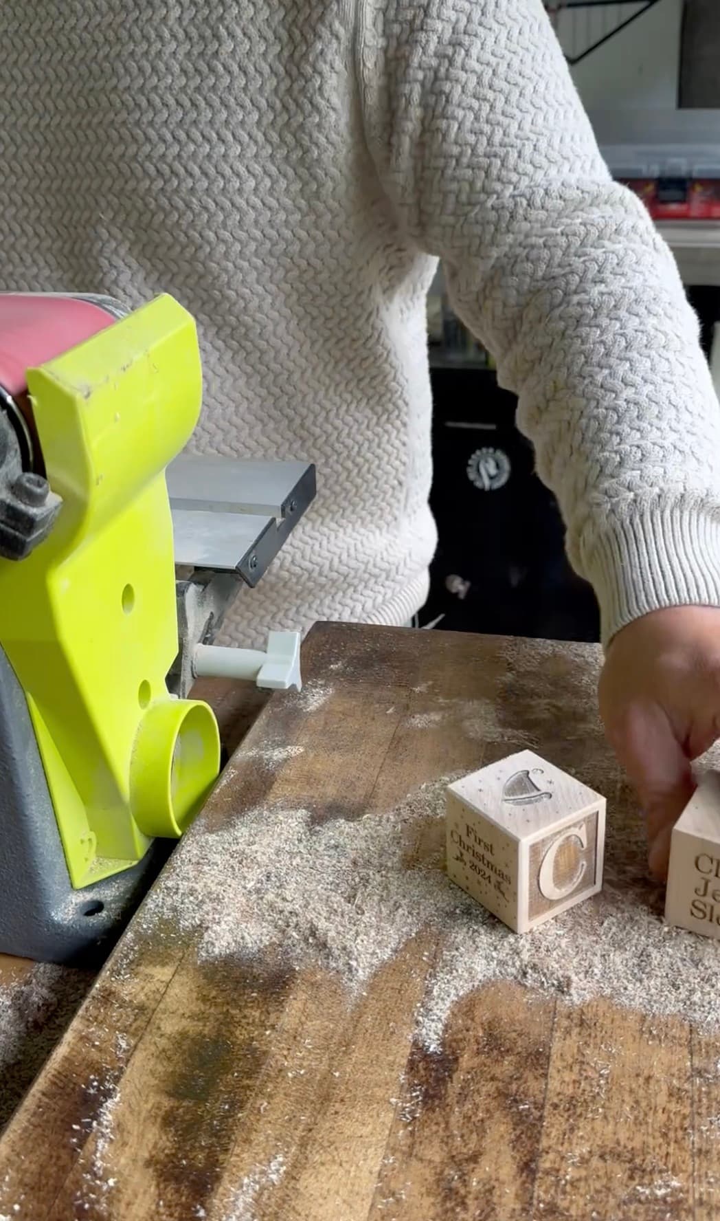 Kirk sanding a freshly engraved First Christmas block at the workshop bench, sawdust covering the table