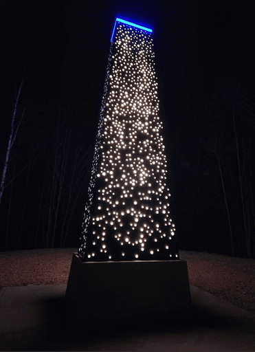 The Ad Astra monument lit up at night, with hundreds of star-shaped perforations glowing from within