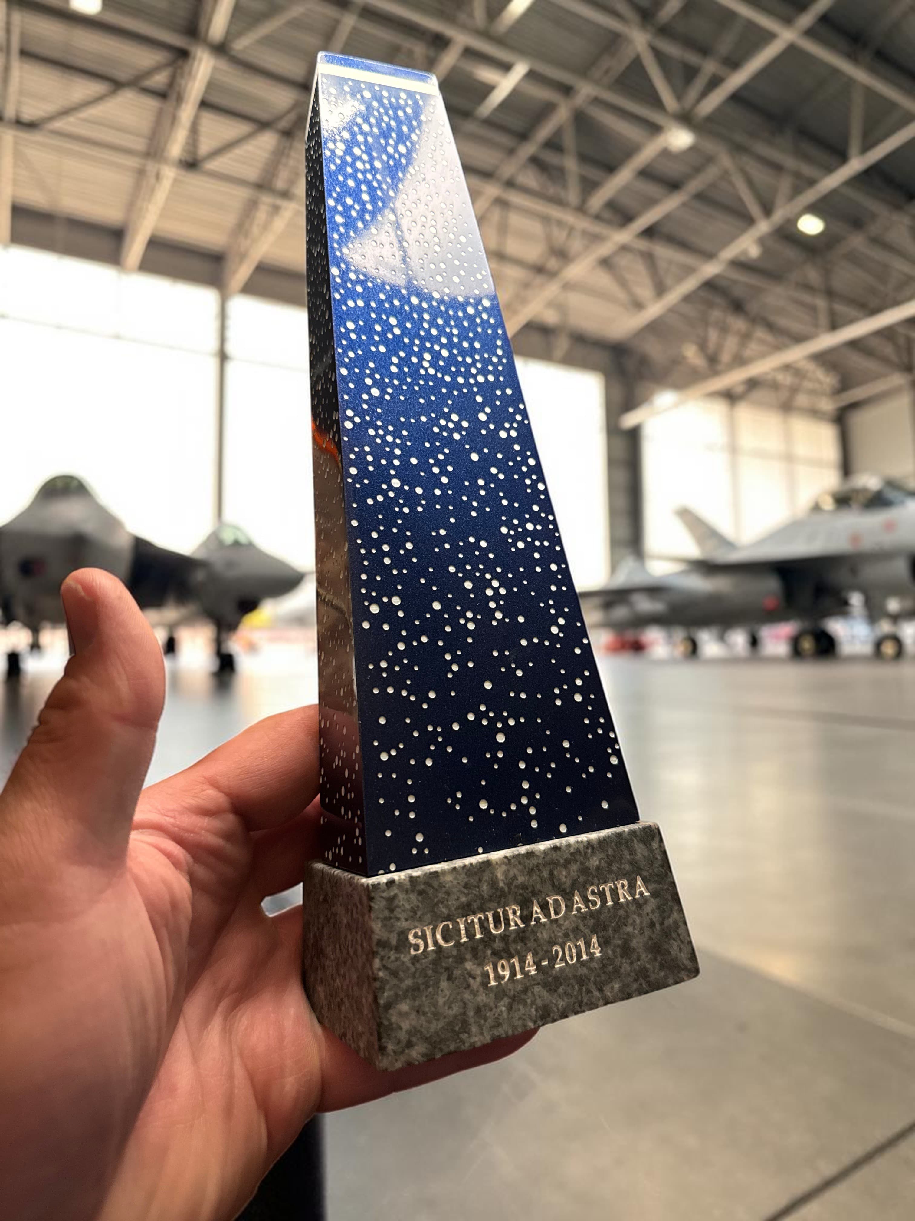 The desk-scale Ad Astra monument replica held inside an RCAF hangar with fighter jets in the background