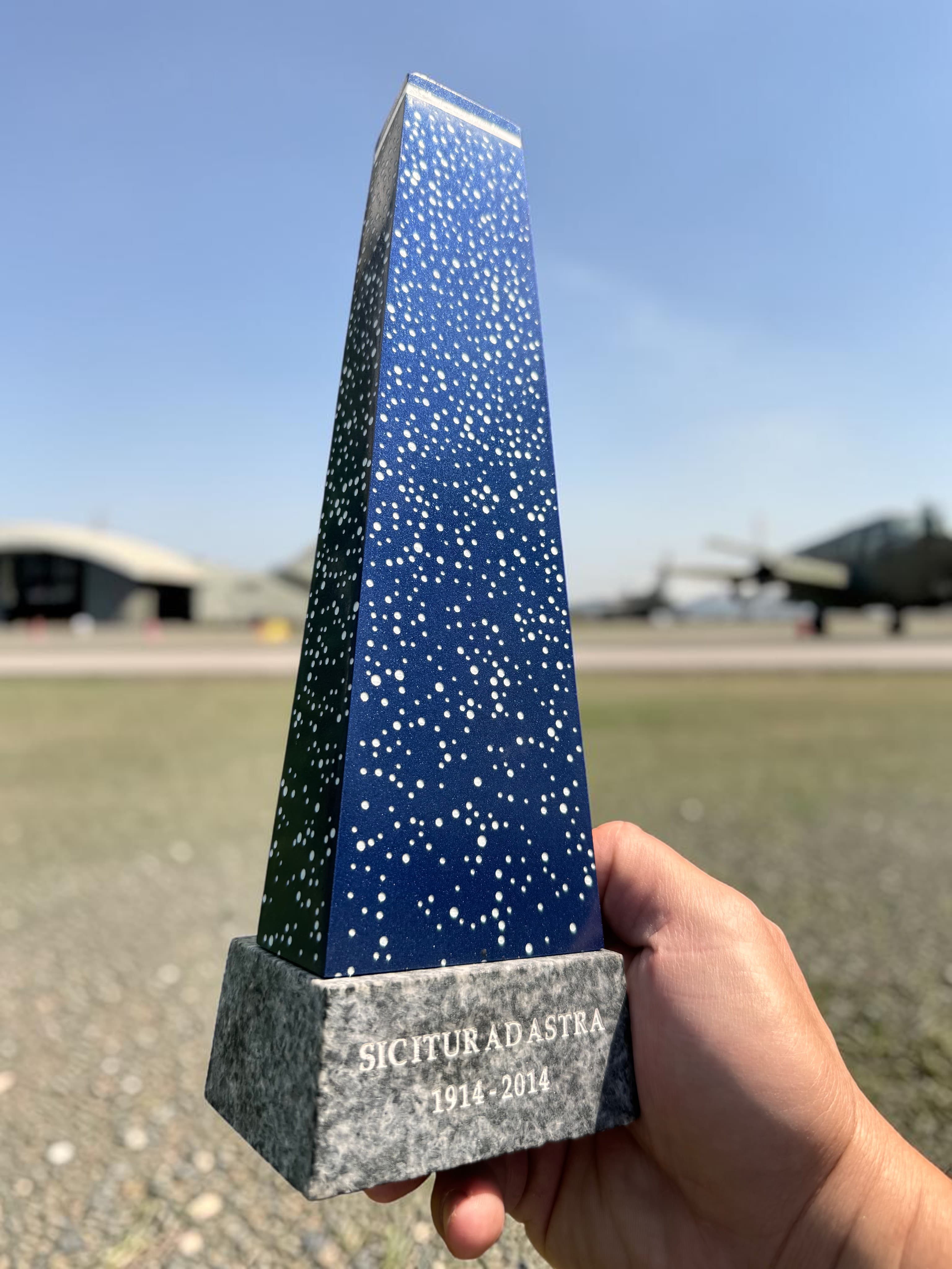 The finished desk-scale Ad Astra monument replica, held outdoors with the actual CFB Borden runway in the background