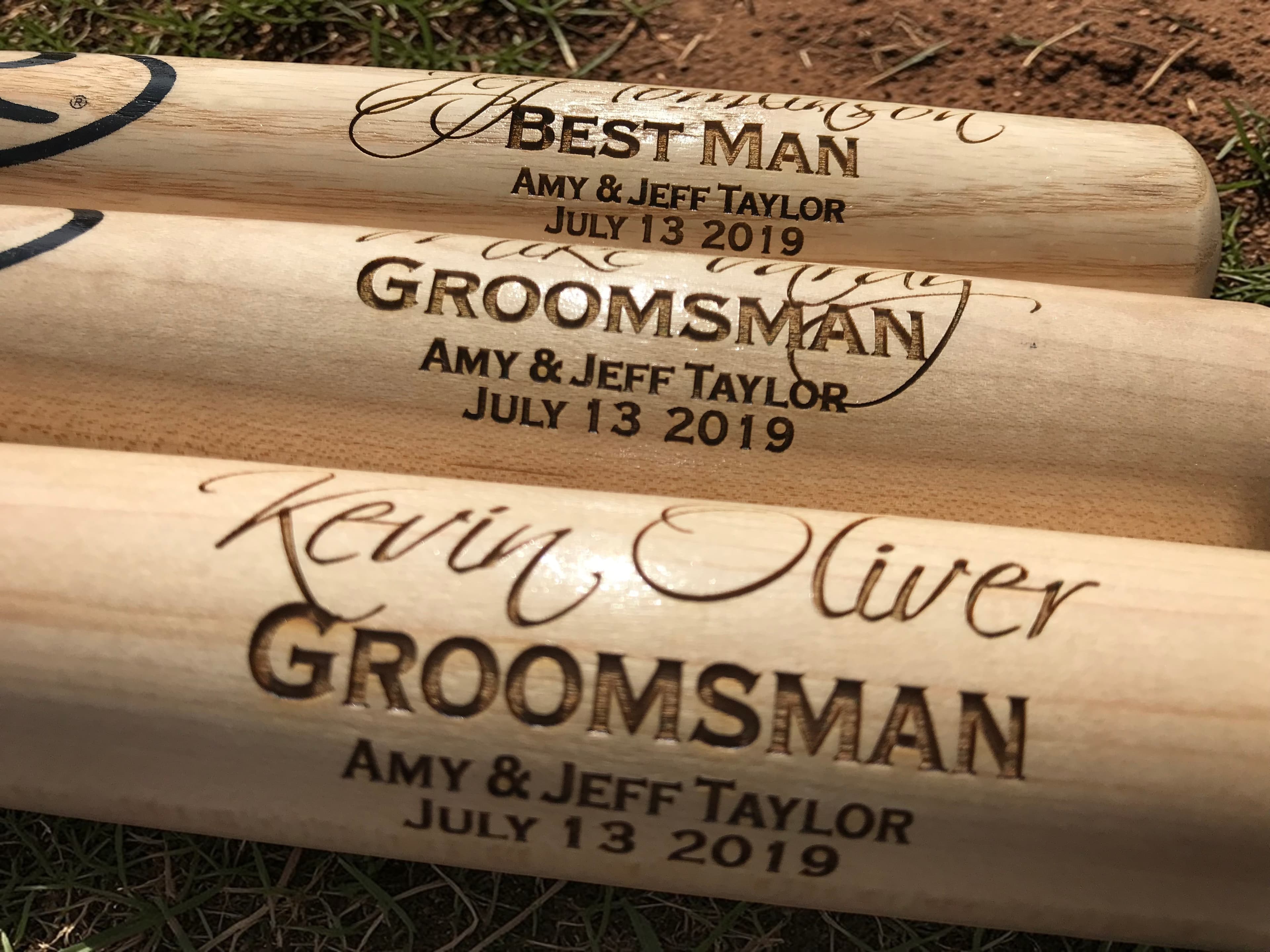 Close-up of laser engraving detail showing Best Man and Groomsman text with signatures on mini baseball bats