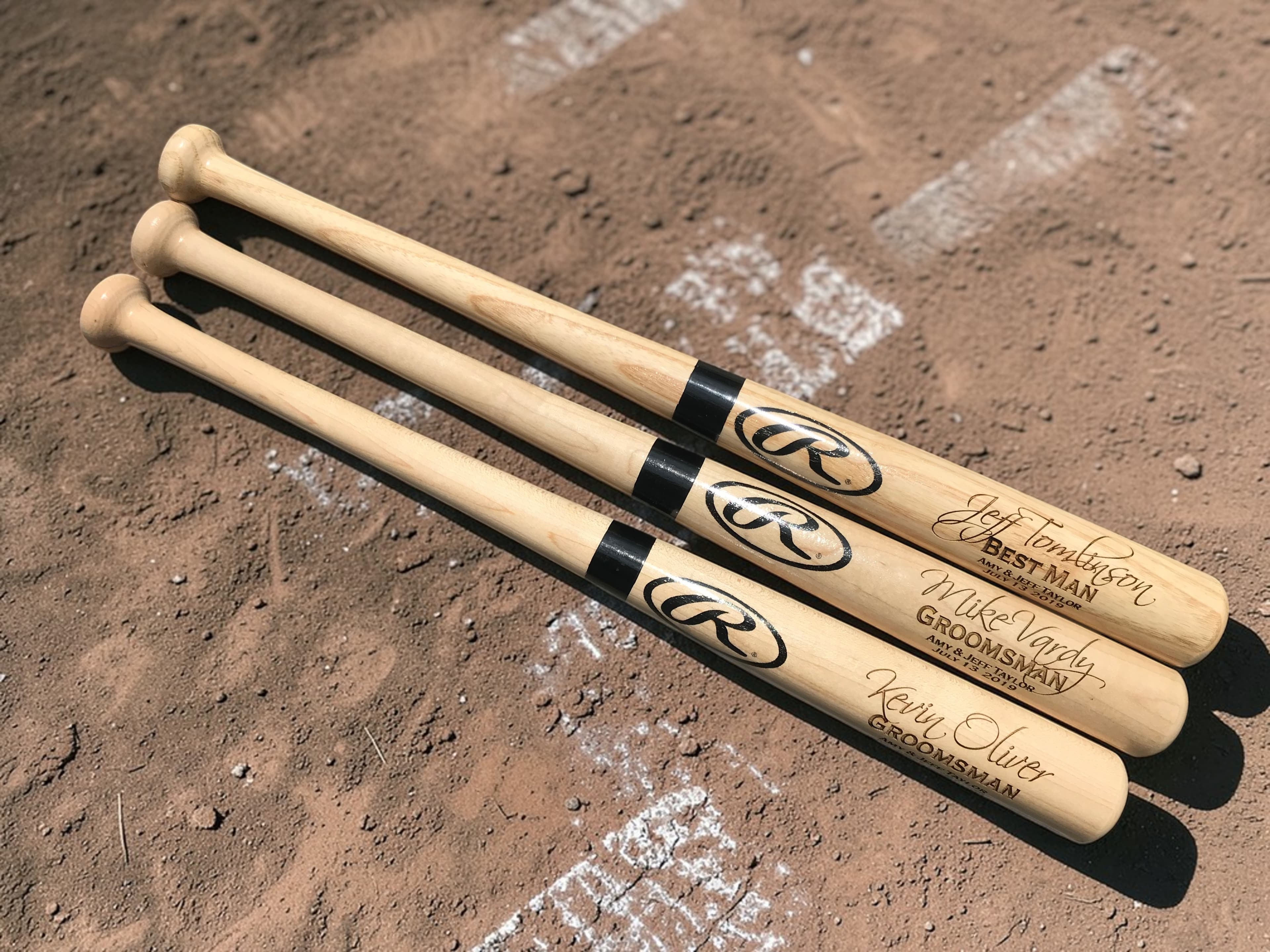 Three engraved Rawlings mini baseball bats on a baseball diamond with chalk baseline visible