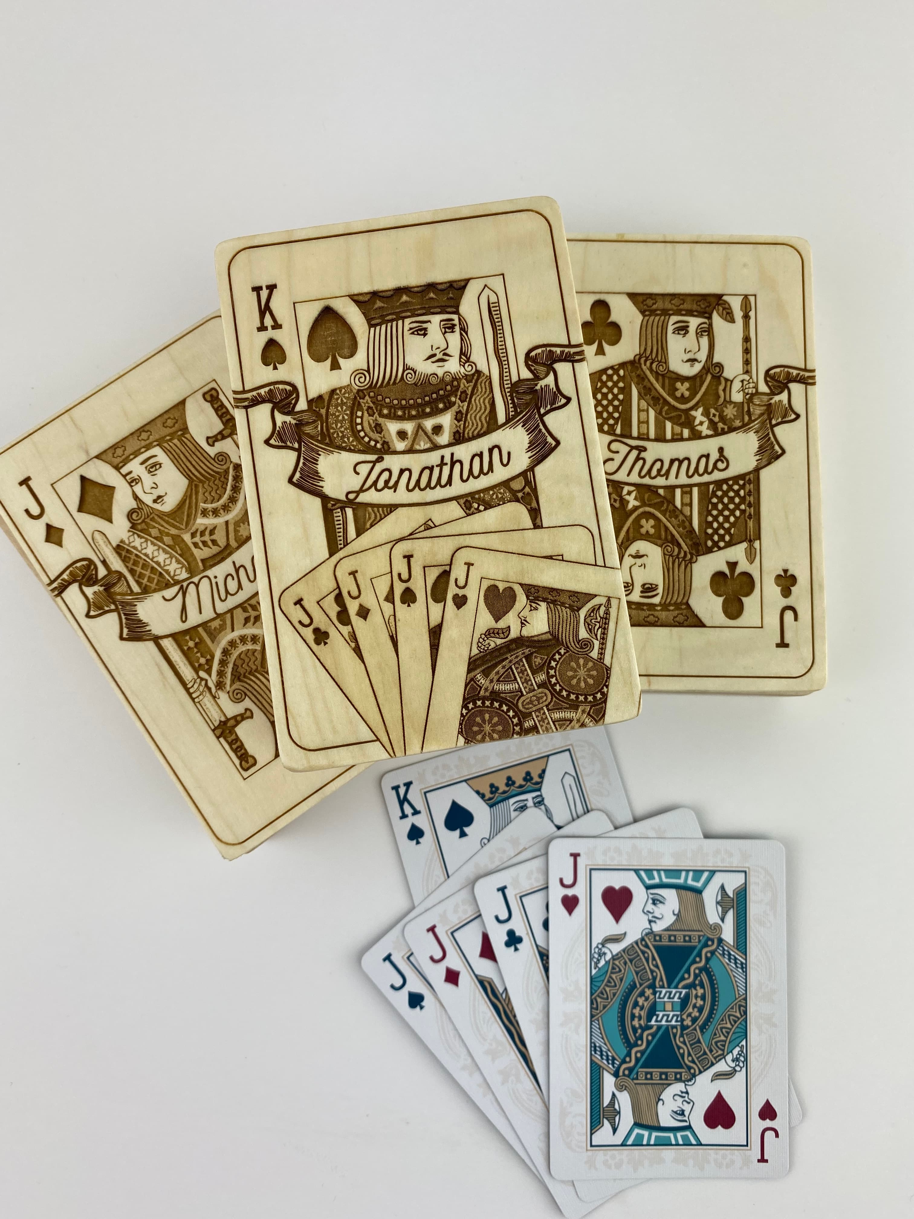 Open playing card box with cards spilling out, engraved lid beside it showing custom artwork