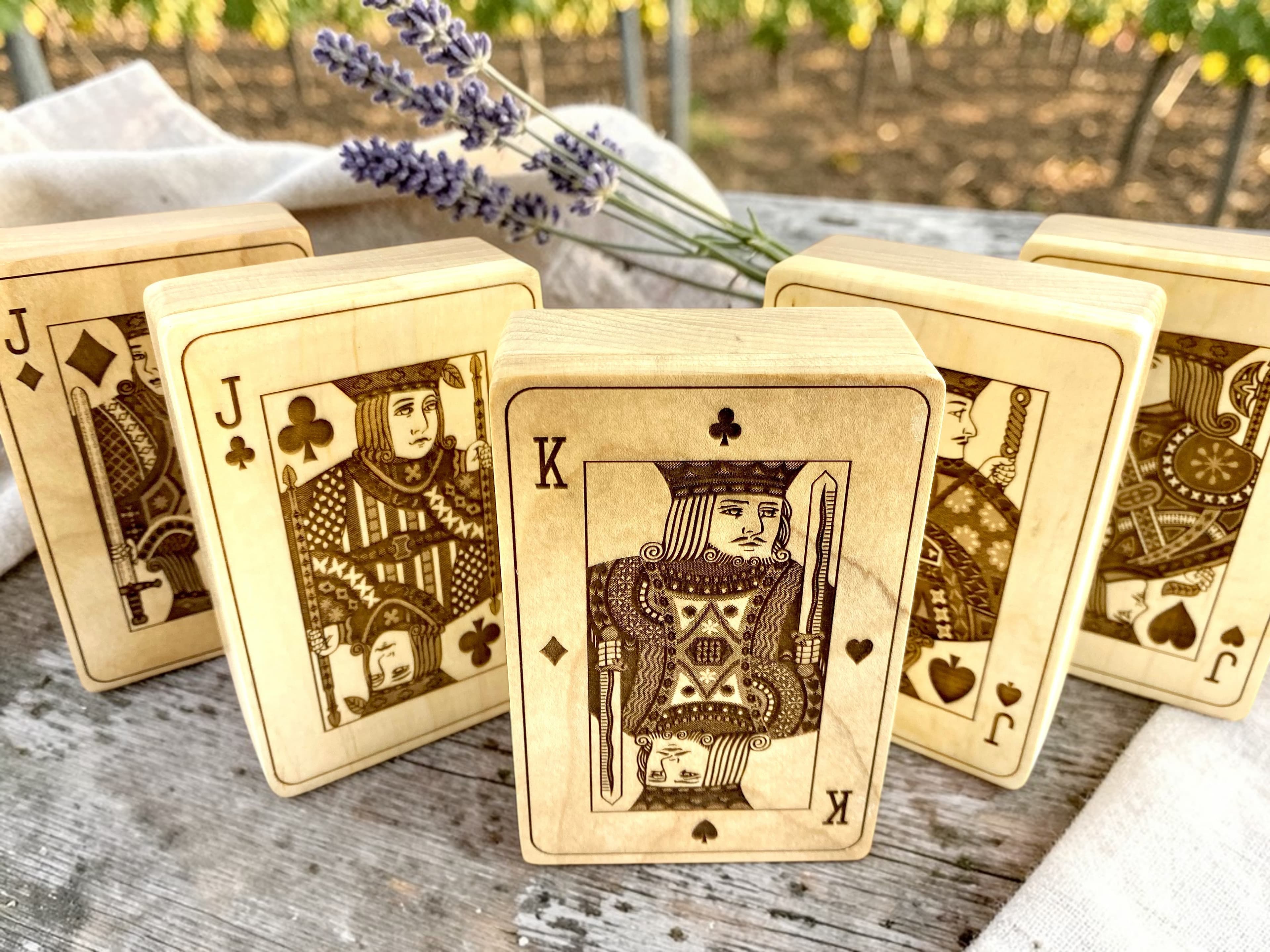 Five engraved playing card boxes on a rustic farm table with lavender and a vineyard in the background