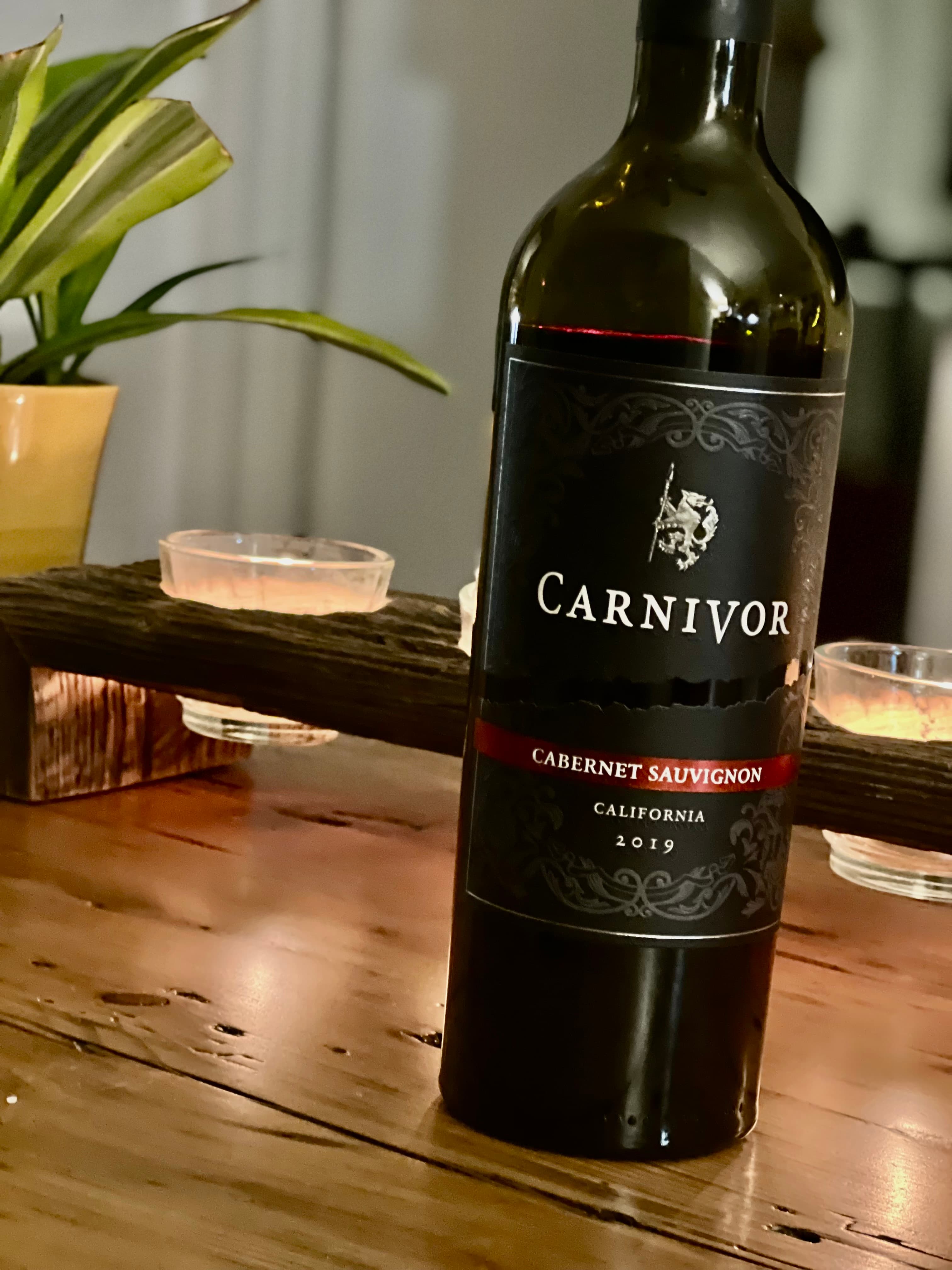 Bottle of Carnivor Cabernet Sauvignon 2019 on a wooden surface with candles