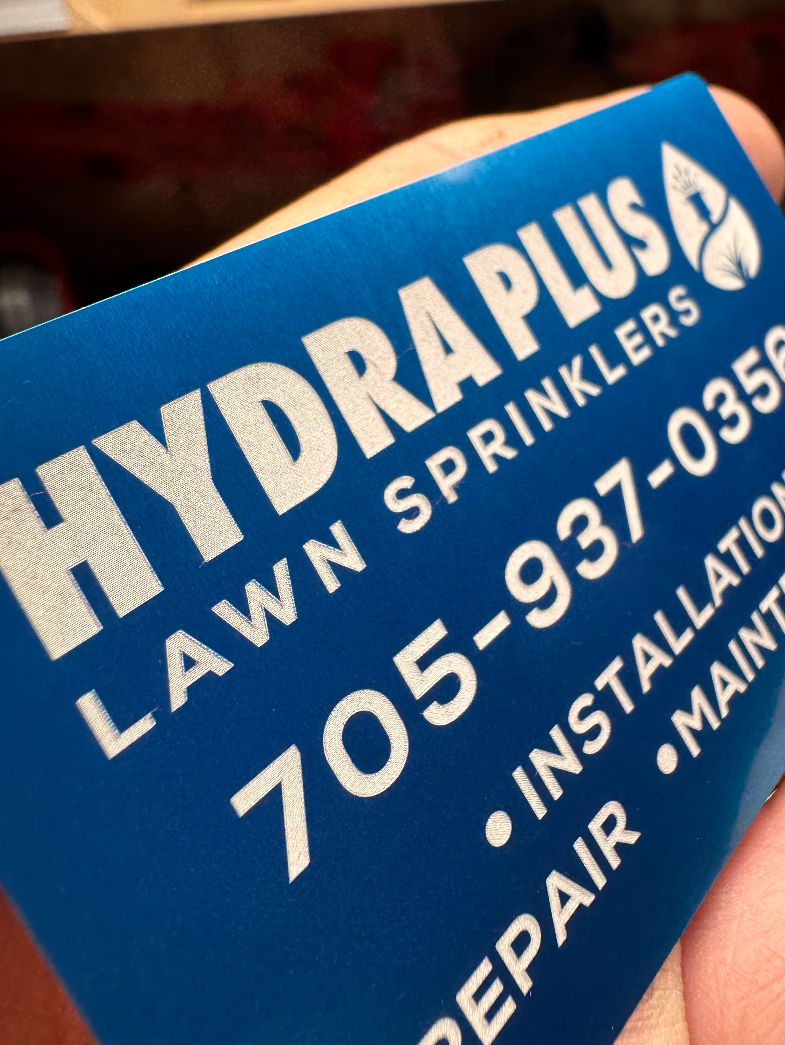 Macro close-up of the laser engraved Hydra Plus Lawn Sprinklers business card, held in hand